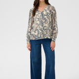 Woman wearing a patterned blouse and blue jeans on a white background