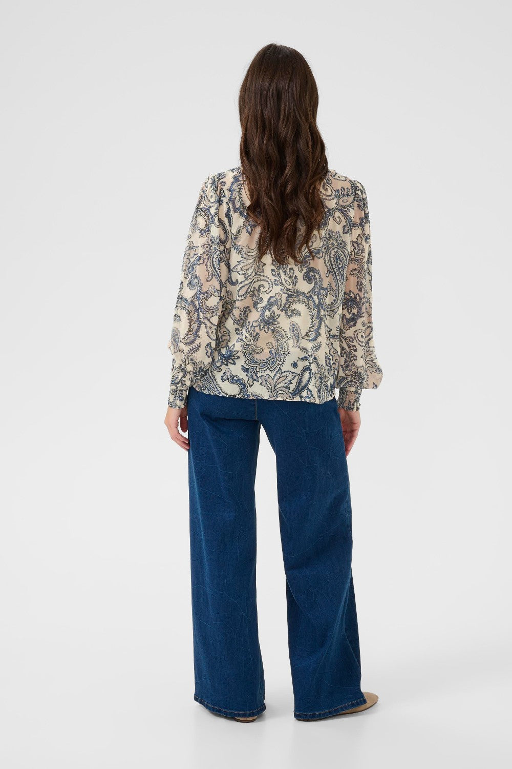 Person wearing a patterned blouse and blue jeans on a white background