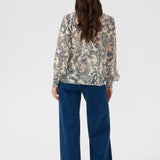 Person wearing a patterned blouse and blue jeans on a white background