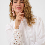 Woman wearing a white blouse with lace details on a plain background