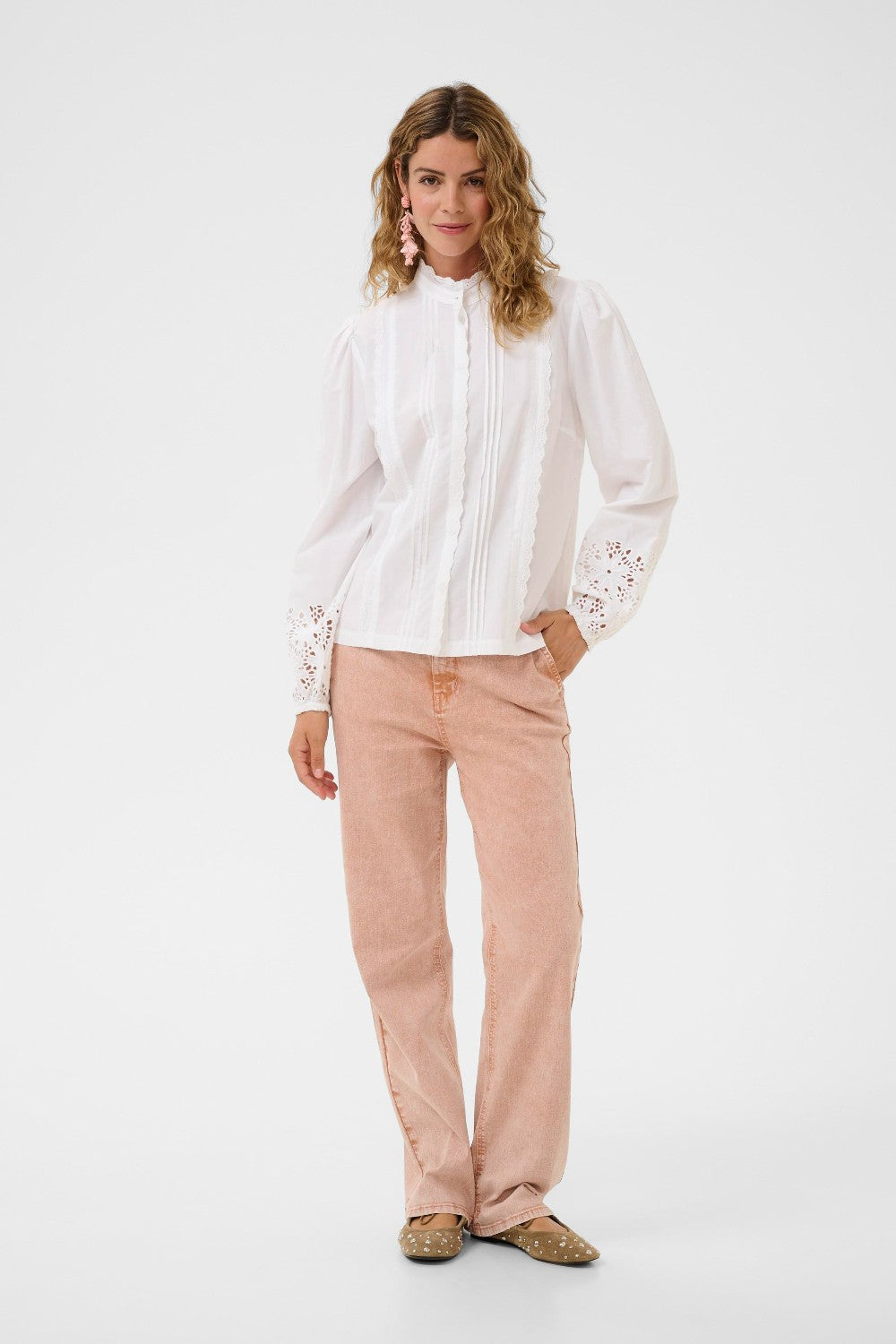 Woman wearing a white blouse with lace details and pink pants on a white background