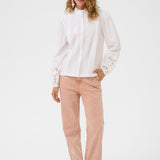 Woman wearing a white blouse with lace details and pink pants on a white background