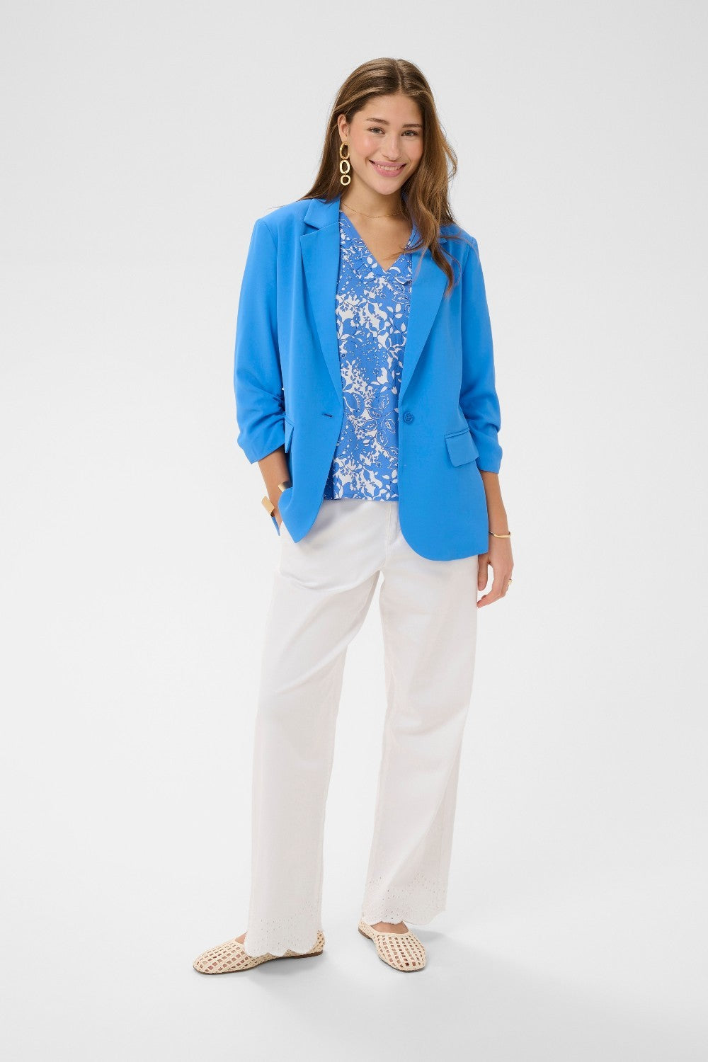 Woman wearing a blue blazer, floral top, and white pants on a white background