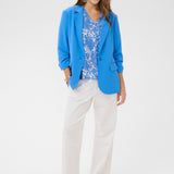 Woman wearing a blue blazer, floral top, and white pants on a white background
