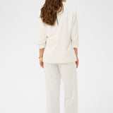 Woman wearing a white blazer and white pants on a light gray background