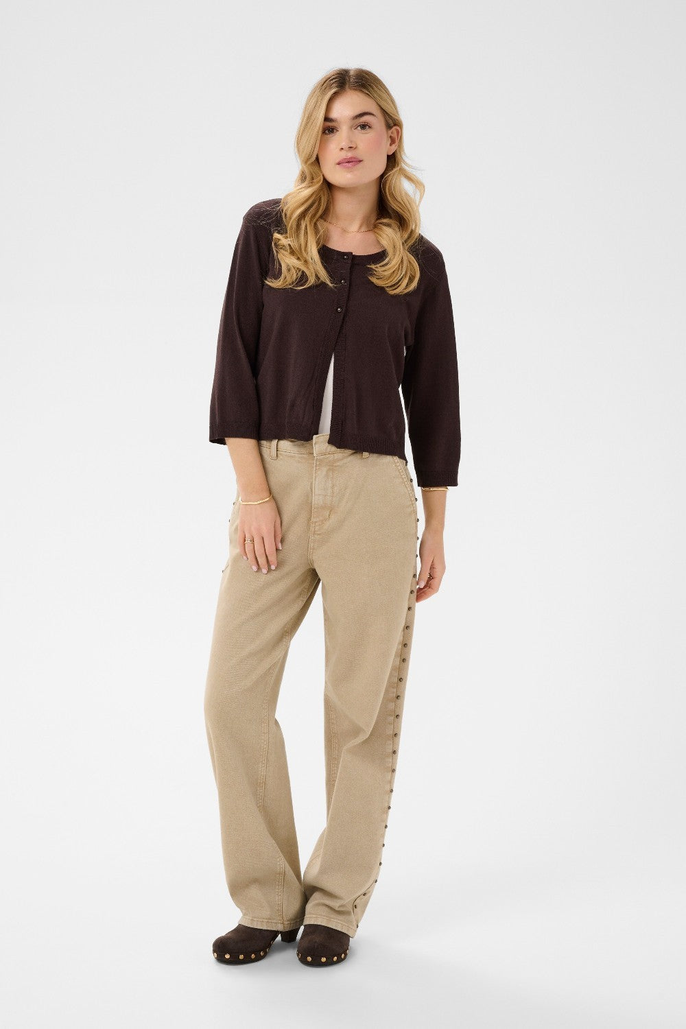 Woman wearing a brown cardigan and beige pants on a white background