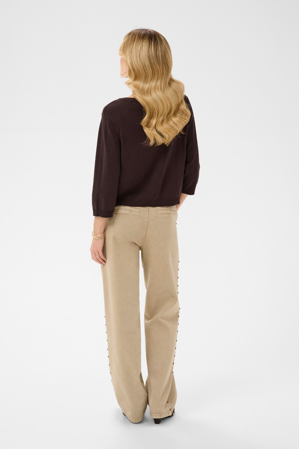 Woman wearing a brown sweater and beige pants on a white background