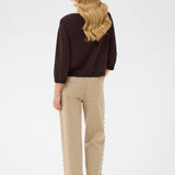 Woman wearing a brown sweater and beige pants on a white background