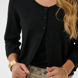 Person wearing a black cardigan with gold jewelry on a white background