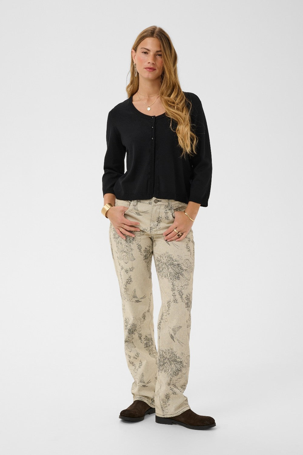 Woman wearing a black cardigan and patterned pants on a white background
