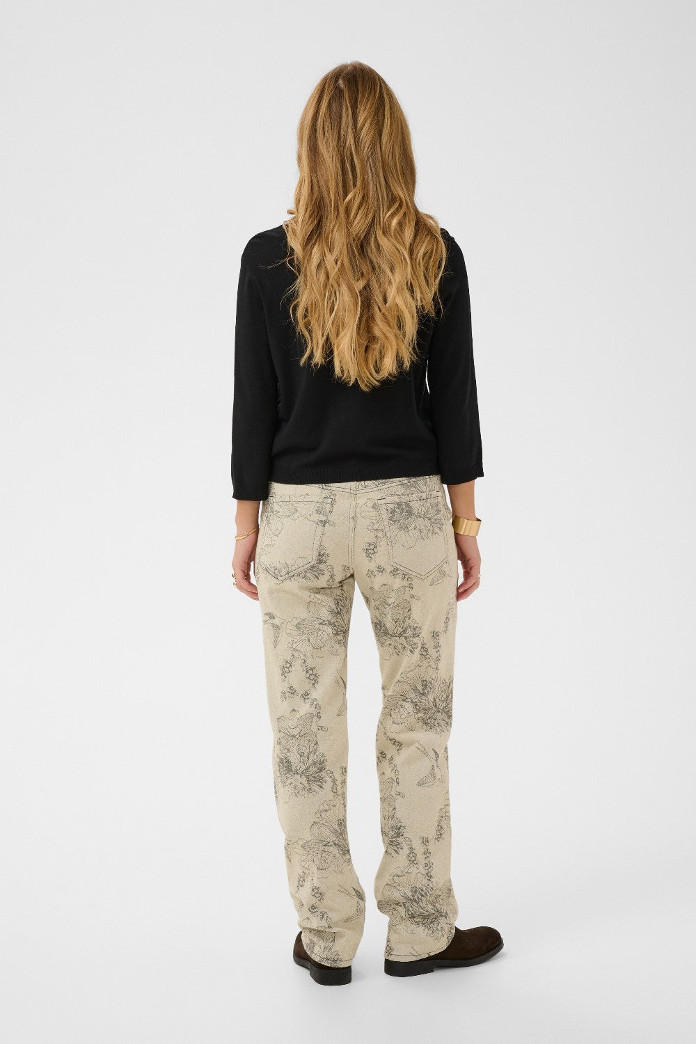 Person wearing a black top and beige patterned pants on a white background