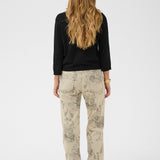 Person wearing a black top and beige patterned pants on a white background