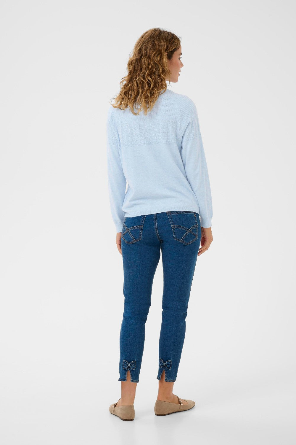 Woman wearing a light blue sweater and dark blue jeans on a white background