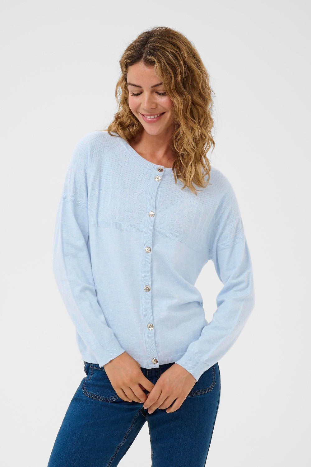 Woman wearing a light blue cardigan and dark blue jeans on a white background