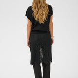 Person wearing a black top and black lace skirt on a white background