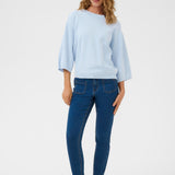 Woman wearing a light blue sweater and dark blue jeans on a white background