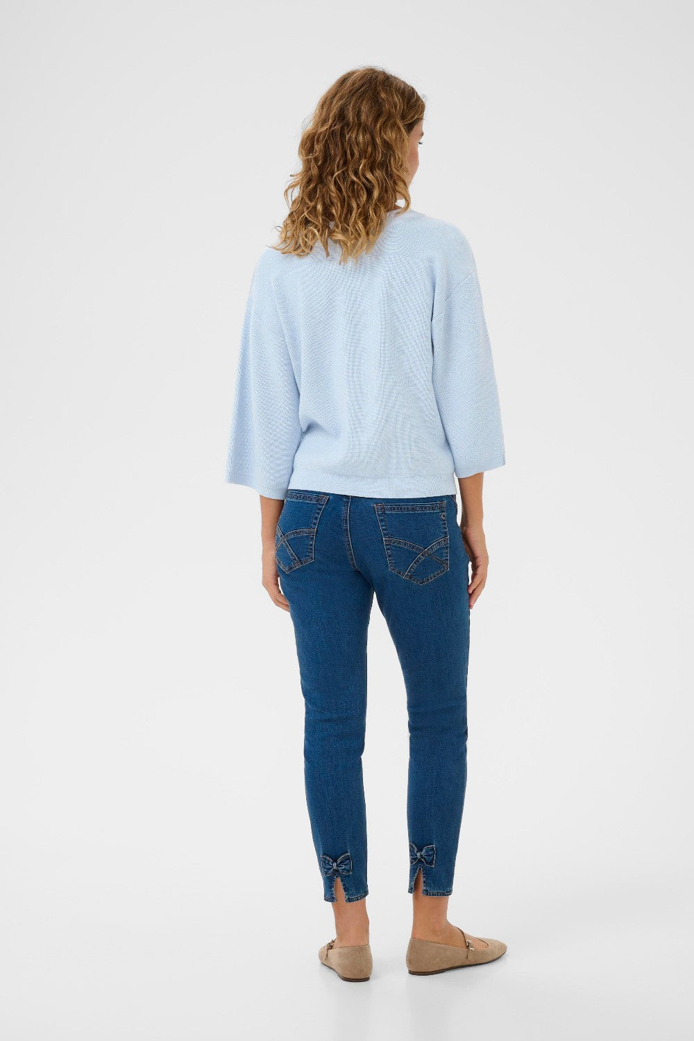 Woman wearing a light blue sweater and dark blue jeans on a white background