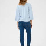 Woman wearing a light blue sweater and dark blue jeans on a white background