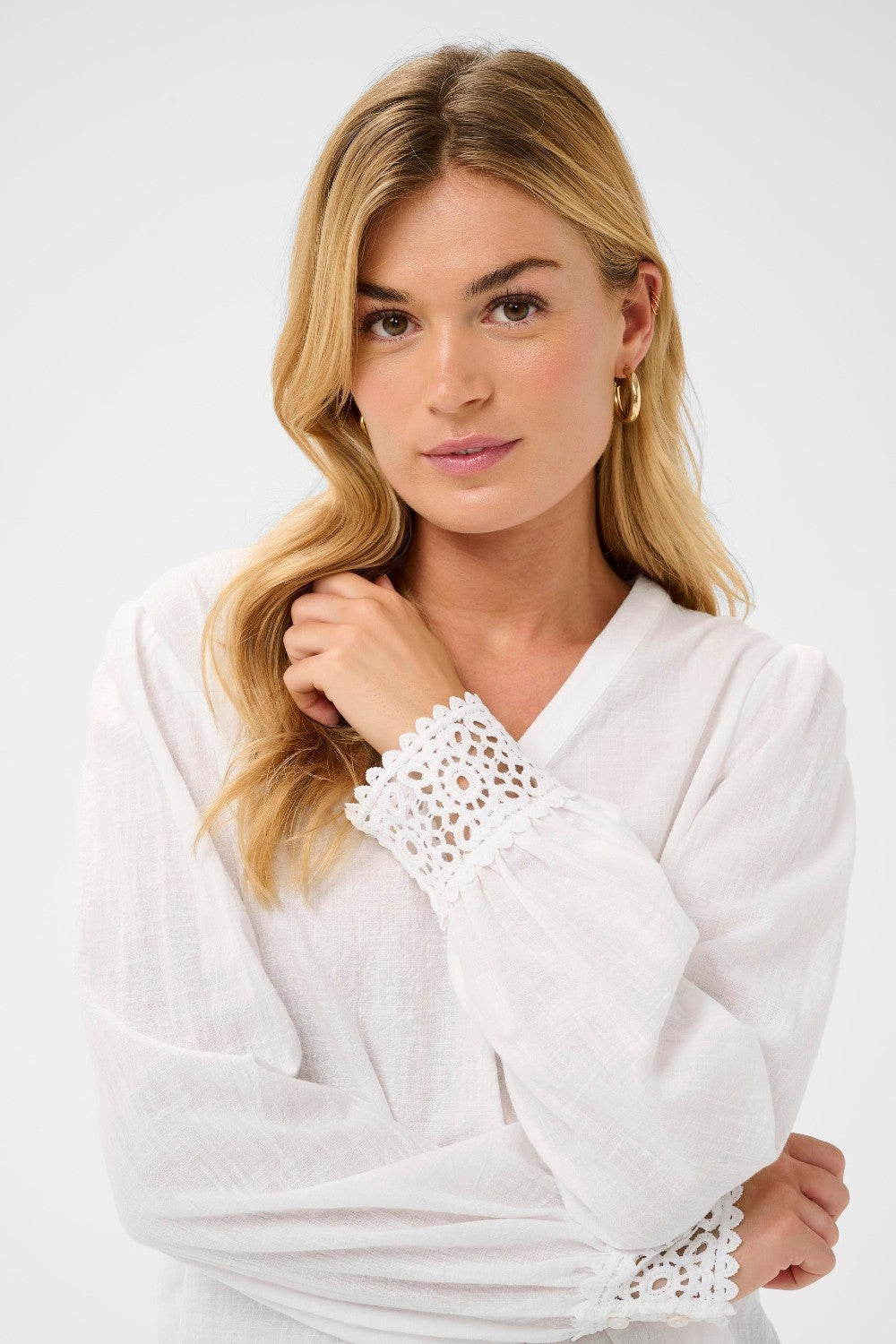 Woman wearing a white blouse with lace details on a plain background
