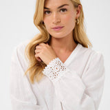 Woman wearing a white blouse with lace details on a plain background