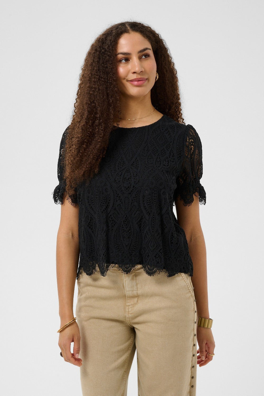 Woman wearing a black lace top and beige pants on a white background