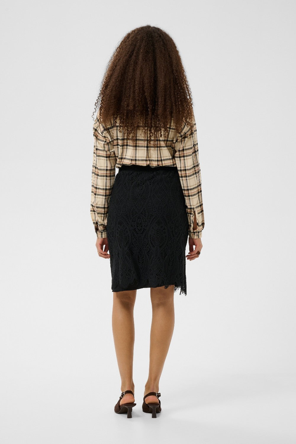 Person wearing a plaid shirt and black skirt from behind on a white background