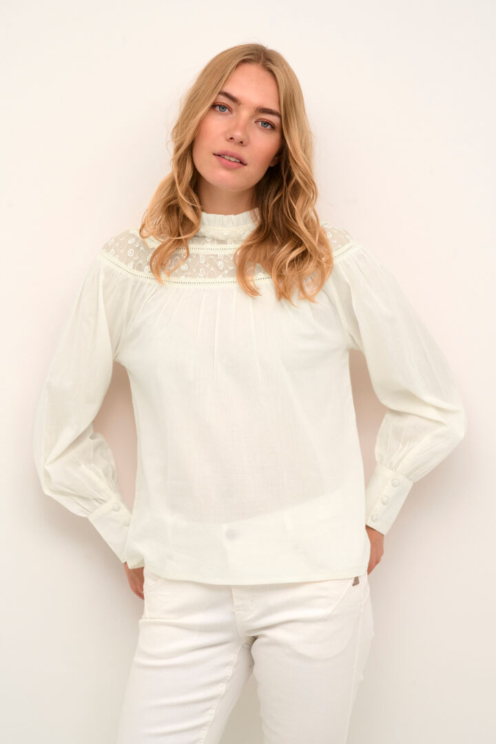 Elevate your wardrobe with our Cream Fio Blouse. The romantic style, cotton body, and beautiful nylon detail at the neck add a touch of sophistication to any look. The key hole with small covered button closure and subtle ruffle at the neck make this blouse a must-have for any fashion-forward individual.