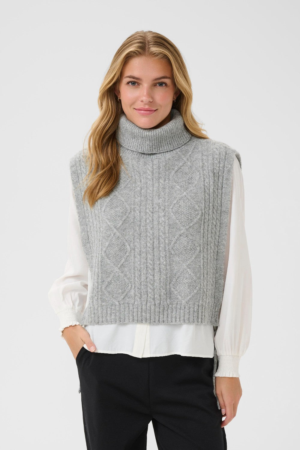 Woman wearing a gray knitted vest over a white shirt on a light gray background