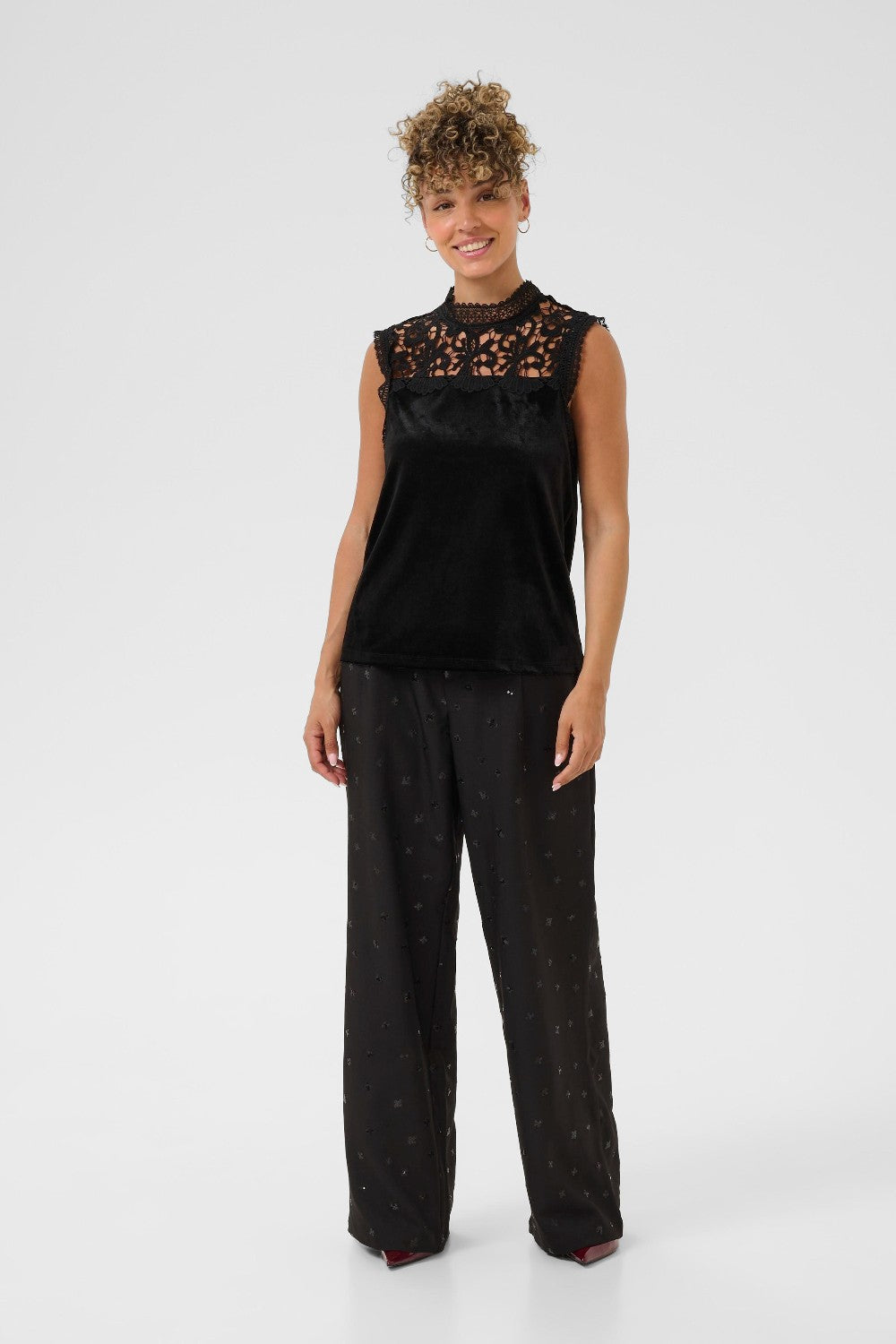 Woman wearing a black sleeveless top with lace details and black pants on a white background