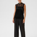 Woman wearing a black sleeveless top with lace details and black pants on a white background