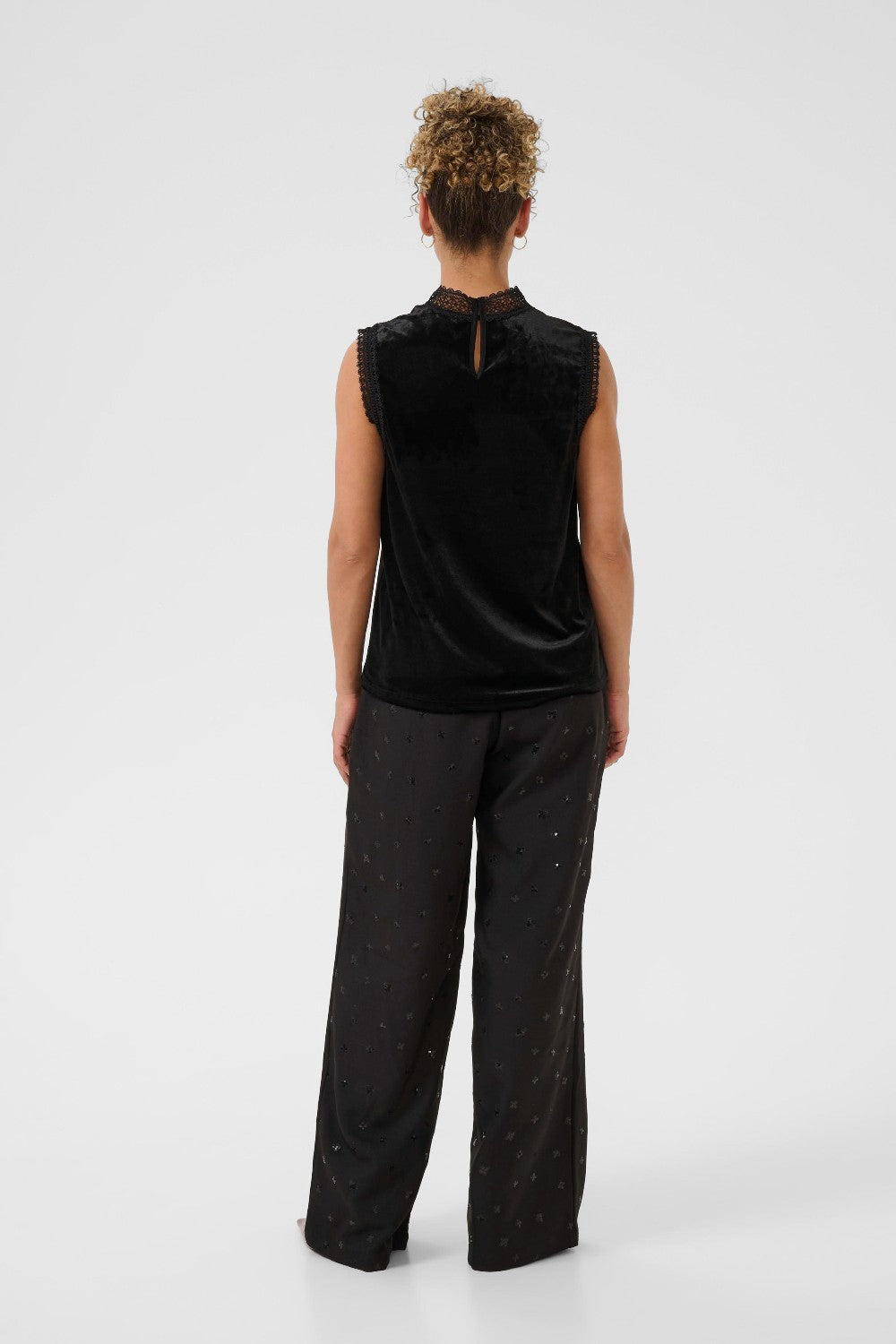 Person wearing a black sleeveless top and dark pants on a white background