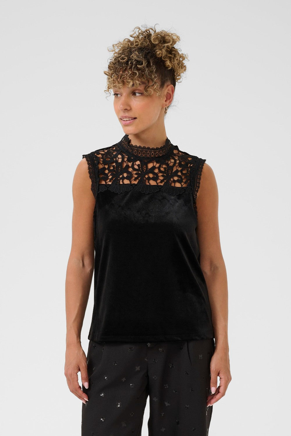 Woman wearing a black sleeveless top with lace detailing on a white background