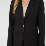 Person wearing a black blazer over a patterned top on a white background