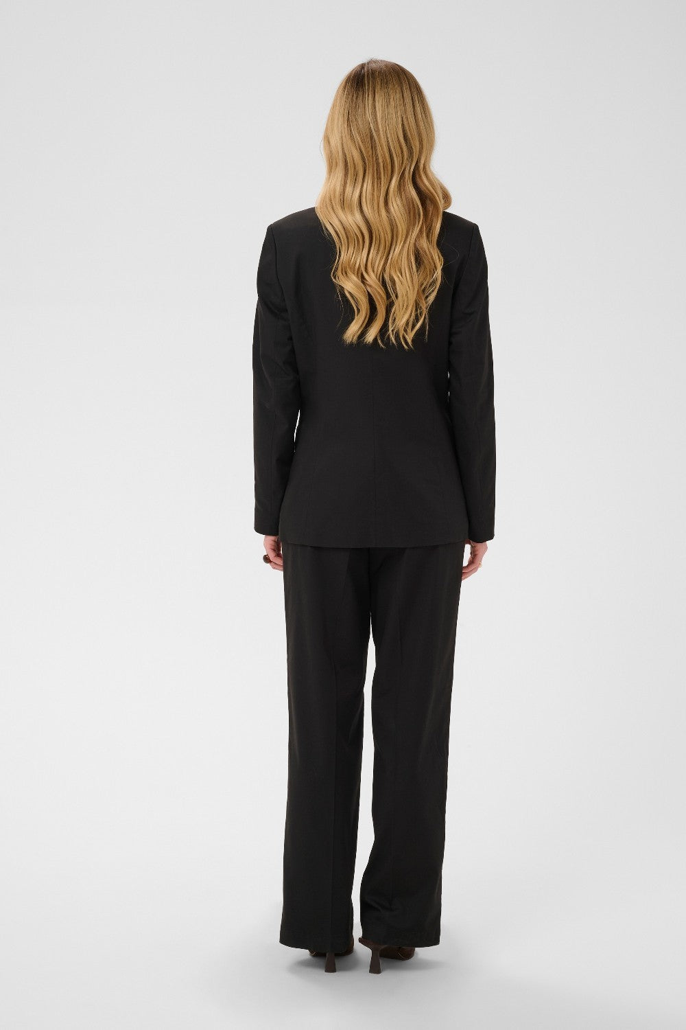 Person wearing a black suit standing against a white background