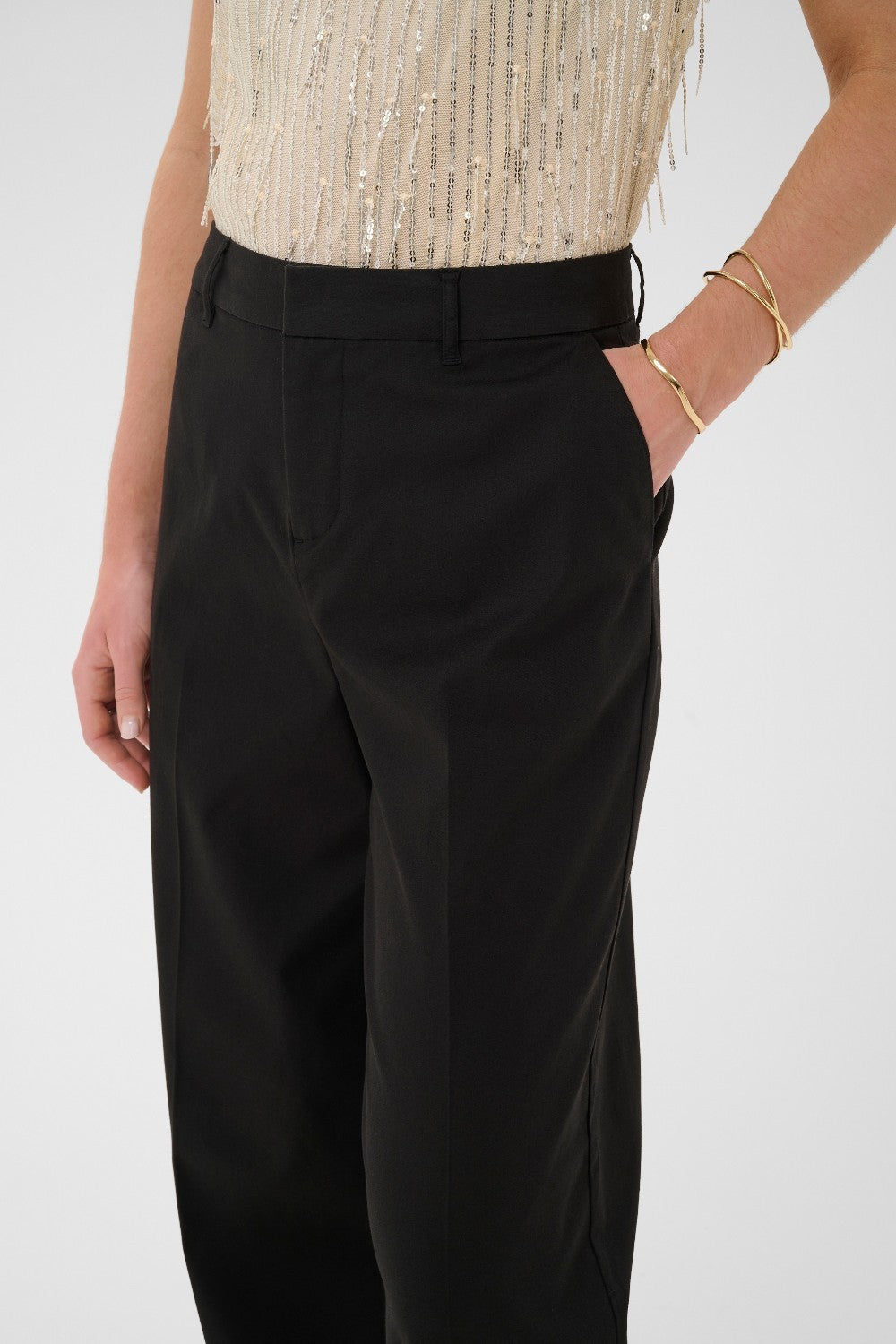 Black pants worn with a gold sequin top on a white background