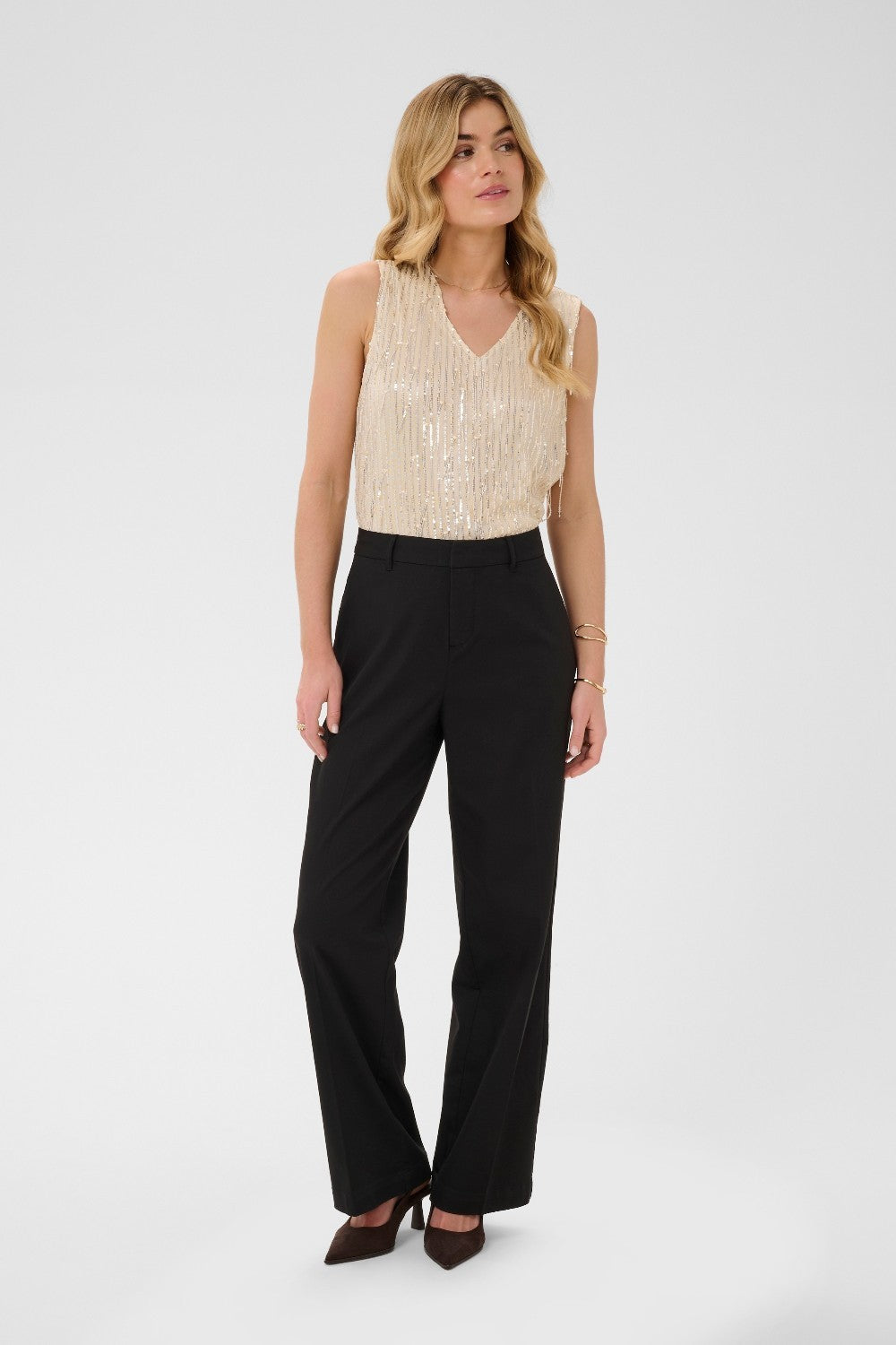 Woman wearing a beige sleeveless top and black pants on a white background