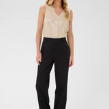 Woman wearing a beige sleeveless top and black pants on a white background