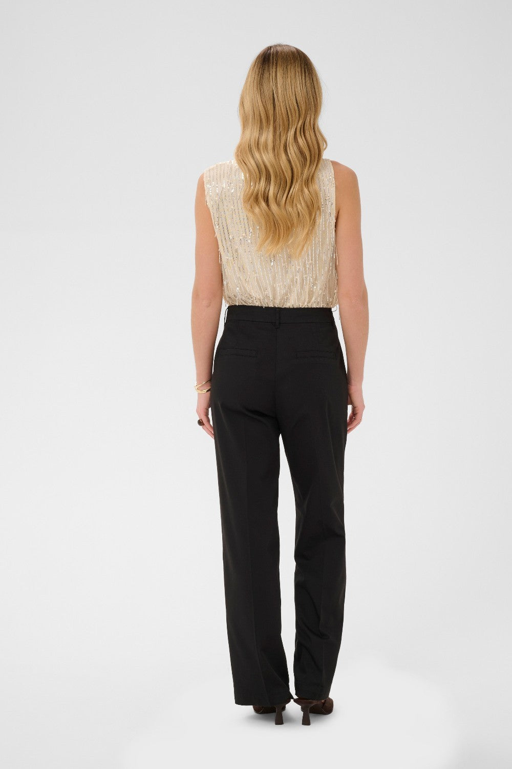 Woman wearing a beige sleeveless top and black pants on a white background
