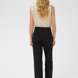 Woman wearing a beige sleeveless top and black pants on a white background