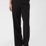 Person wearing black pants and a beige top on a white background