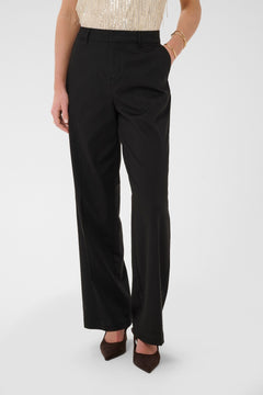 Person wearing black pants and a beige top on a white background