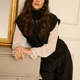 Woman in a stylish outfit with a black top and white sleeves leaning against a fireplace.