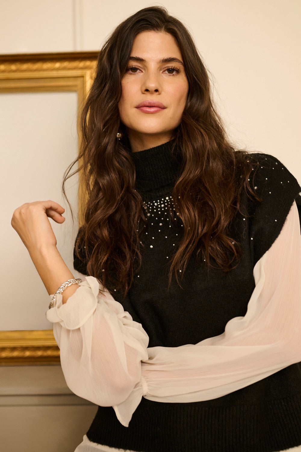 Woman wearing a black top with sheer sleeves against a neutral background