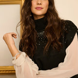 Woman wearing a black top with sheer sleeves against a neutral background
