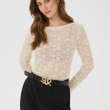 Woman wearing a beige lace top and black pants with a gold belt on a white background