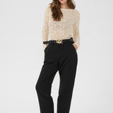 Woman wearing a beige sweater and black pants on a white background