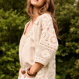Woman wearing a beige blouse and white pants with a crochet cover-up in a natural setting