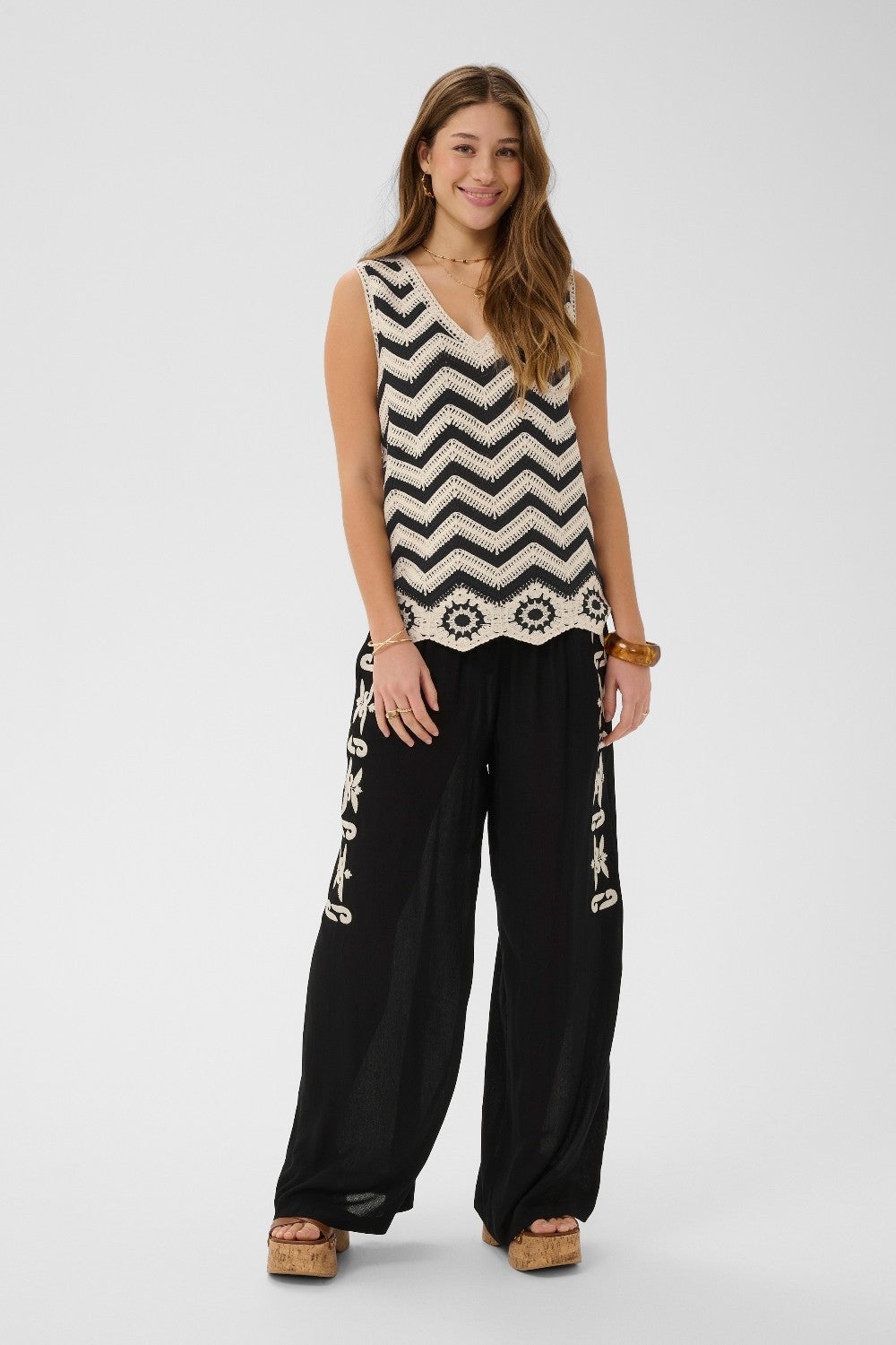 Woman wearing a sleeveless top with a zigzag pattern and black pants with white designs on a white background