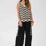 Woman wearing a sleeveless top with a zigzag pattern and black pants with white designs on a white background