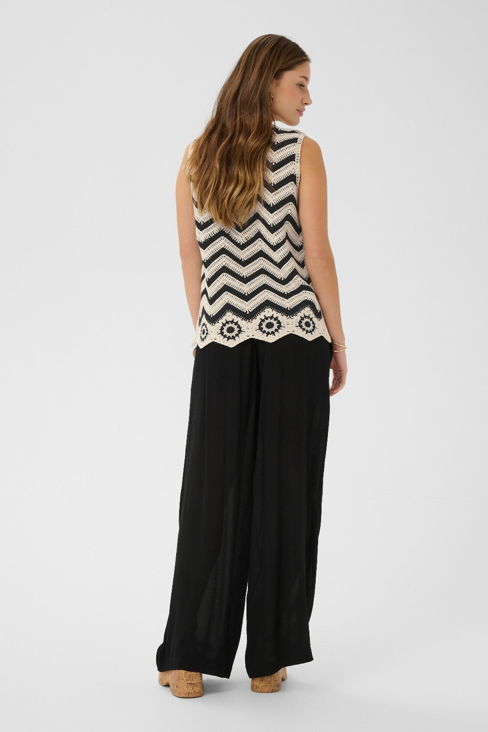 Woman wearing a sleeveless black and white patterned top with wide-leg pants on a white background
